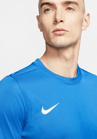 Blauwe sportshirt gemaakt van gladde stof, met een ronde hals en een wit Nike-logo op de linkerborst. Close-up weergave.