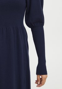 Tjocktröja i marinblått med en åtsittande bodice, puffärmar och texturerade ribbade muddar. Mjukt, slätt tyg med en avslappnad silhuett.