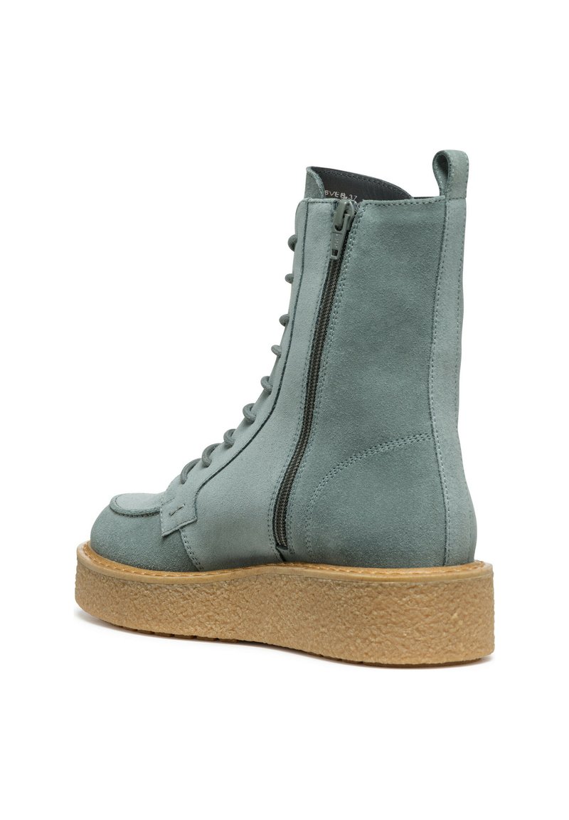 Bottine en suède gris avec un bout rond, fermeture éclair sur le côté et semelle à motifs. Caractéristiques des accents découpés en cercle et une semelle épaisse texturée.