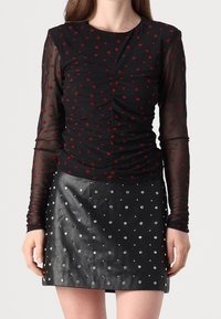 Svart långärmad topp med röda hjärtmönster, veckad detaljering och rund halsringning, i kombination med en svart läder minikjol med silvernitar.