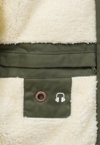Green fabric with a soft white fleece lining, featuring a headphone logo and a brown metal eyelet. Zipper pocket included for storage.