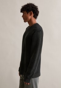 Tmavě šedý žebrovaný svetr s kulatým výstřihem, dlouhými rukávy a texturovanou tkaninou, v páru se šedými kalhotami, z profilu.