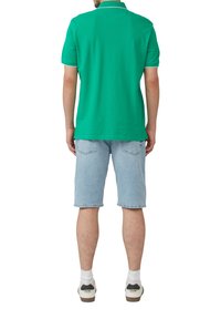 Zielona koszulka polo z kołnierzykiem, zestawiona z jasnoniebieskimi szortami dżinsowymi i białymi trampkami z ciemnym akcentem przy pięcie.