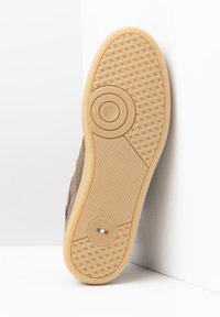 Braune Wildledersohle mit einer strukturierten Gummiaußensohle, die ein kreisförmiges Design und ein Markenlogo trägt. Einheitliche beige Farbe mit detaillierten Grip-Mustern.