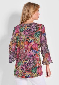 Durchsichtige Bluse mit einem lebhaften Blumenmuster in Pink-, Lila- und Grüntönen. Dreiviertelärmel mit Rüschensaum und einem runden Ausschnitt.