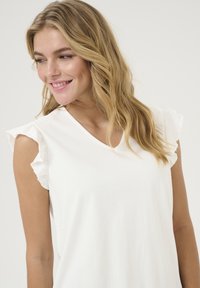 Haut blanc en v allant en douceur, fabriqué en tissu doux, avec des manches courtes froncées et une coupe décontractée. Texture lisse avec un design uni.