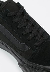 Baskets noires avec une tige en daim et toile, lacets plats noirs, semelle en caoutchouc et un logo sur le côté de couleur noire assortie.