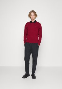 Sweater bordô com gola preta, mangas longas e ajuste slim. Calças escuras e botas pretas completam o conjunto. Design minimalista com detalhe do logo.