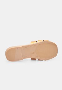 Sandalo piatto con una tomaia sintetica liscia di color marrone chiaro e una suola in gomma beige testurizzata. Presenta due cinghie sovrapposte.