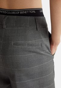 Szare spodnie w kratę z czarnym pasem z napisem "UNITED COLORS OF BENETTON". Teksturowana tkanina, slim fit, z detalem w postaci tylnej kieszeni.