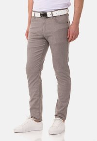 Gestreifte, hellbraune Hosen mit schmaler Passform, aus einem Stoff mit strukturiertem Finish. Kombiniert mit einem weißen Gürtel und weißen Sneakers.