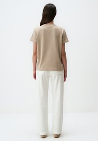 Maglietta in cotone beige a maniche corte, con scollatura a girocollo e vestibilità rilassata, indossata con pantaloni bianchi a gamba larga a vita alta.