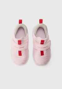 Scarpe da ginnastica rosa chiaro con tomaia in tessuto testurizzato, cinturino elastico, dettagli rossi e tallone imbottito per il comfort. Suola in gomma bianca.