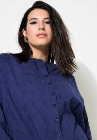 Camicia button-up blu navy con motivo floreale testurizzato, colletto arrotondato e maniche lunghe. Caratterizzata da una vestibilità ampia e bottoni tono su tono.