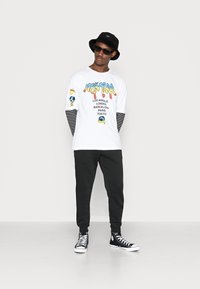 Hvit langermet t-skjorte med fargerik "New York" grafikk; svart og hvit stripete mansjetter. Kombinert med svarte bukser og svarte høye sneakers.