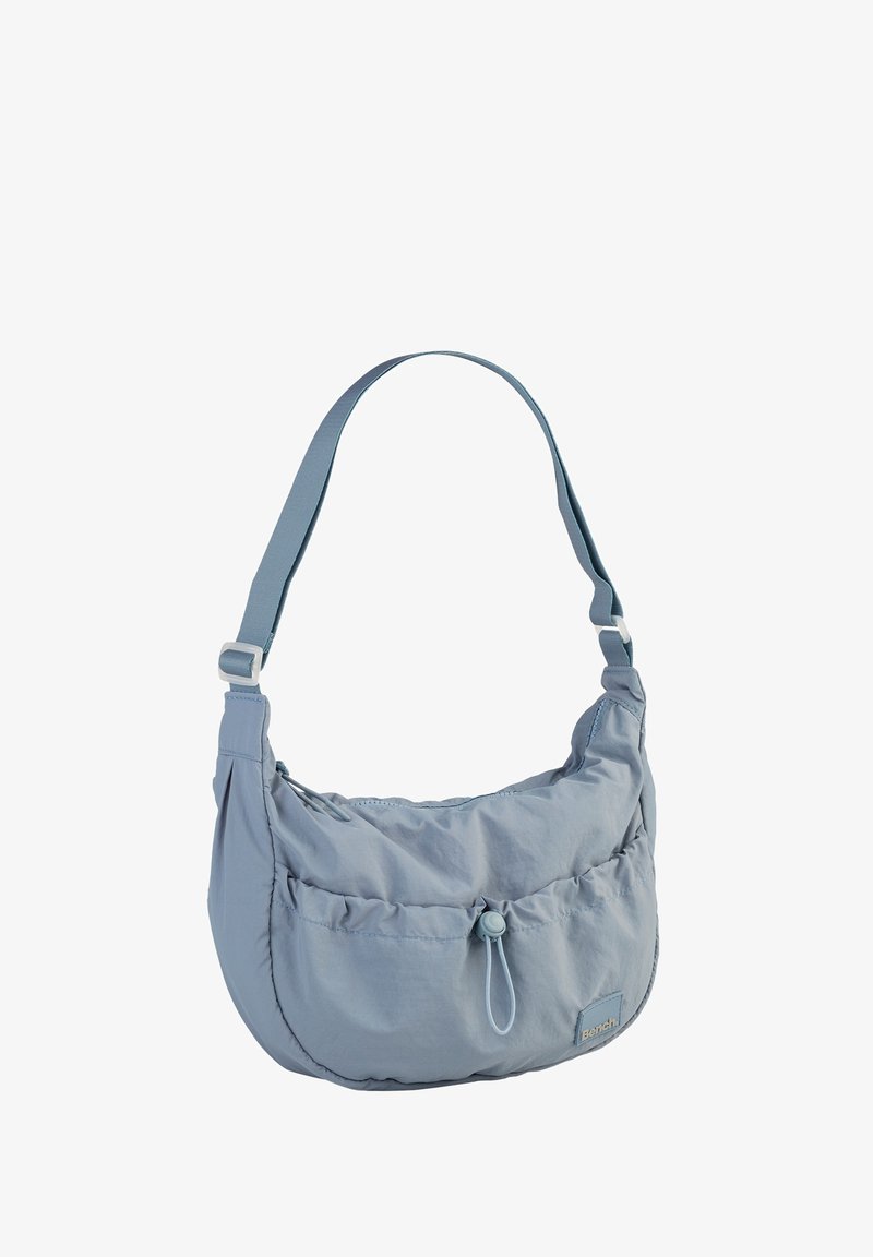 Hellblaue Schultertasche aus einem weichen, strukturierten Stoff. Sie verfügt über eine geraffte Fronttasche, einen verstellbaren Riemen und einen Toggle-Verschluss.