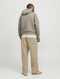 Felpa oversize grigia chiara con tasca posteriore, indossata su un outfit a strati beige, abbinata a pantaloni larghi beige e sandali neutri.