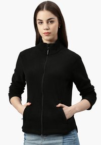 Giacca in pile nera con zip, colletto rialzato, maniche lunghe, tasche laterali e una texture morbida, caratterizzata da elementi di design minimalisti.
