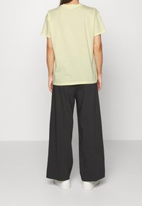 Světle žluté bavlněné tričko s krátkými rukávy, doplněné volnými černými kalhotami. Outfit je doplněn bílými teniskami pro ležérní vzhled.