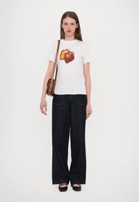 Witte t-shirt met een aardbeienafbeelding, gecombineerd met donkere denim wijde broeken en een bruine schoudertas. Gestructureerde zwarte flats maken de look compleet.