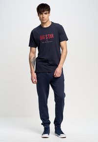 Camiseta de algodón navy con "BIG STAR" impreso en rojo. Combinada con joggers navy a juego y deportivas azules. Diseño simple y casual.