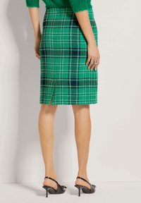 Groene geruite kokerrok met witte en marineblauwe accenten, voorzien van een split aan de achterkant. Draagt bij zwart slingback hakken. Textuurstof.