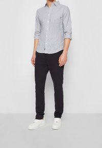 Koszula na guziki w jasnoniebieskie i białe paski z długimi rękawami i kieszenią na piersi, zestawiona z czarnymi spodniami i białymi trampkami.