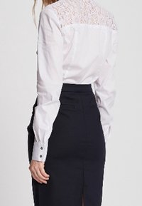 White long-sleeve blouse with lace detail on the back, paired with a form-fitting black skirt featuring a back slit and button accents.