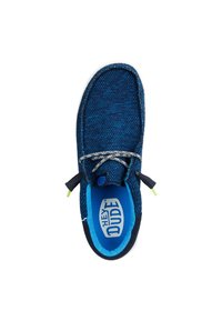 Zapato slip-on de malla azul con un upper texturizado, forro interior en un azul contrastante, suela blanca y cordones decorativos. Cuenta con la marca "HEY DUDE".