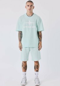 Camiseta de gran tamaño en verde menta con el logo blanco "PXP", combinada con pantalones cortos a juego. Confeccionada con tela suave, presenta un corte holgado y mangas cortas.