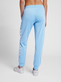 Ljusblåa sweatpants med dragsko i midjan, med vita chevronmönster längs sidorna och elastiska muddar vid anklarna.