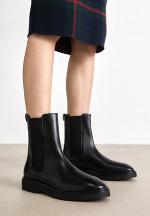 Bottes Chelsea en cuir noir avec panneaux élastiques latéraux, bout pointu et semelle en caoutchouc plate. Texture lisse et design minimaliste.