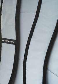 Tirantes de color azul claro con bordes negros, que cuentan con acolchado y un logotipo de Skechers visible. Superficie texturizada con costuras en contraste.