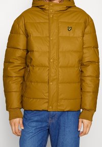 Hnědá péřová bunda s kapucí, vybavená patentkami, žebrovanými manžetami a malým žlutým logem na hrudi. Měkký, texturovaný materiál.