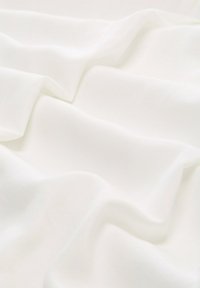 Glatte weiße Stoff mit sanften Falten und sanften Schatten, die eine fließende Textur über die Oberfläche erzeugen.