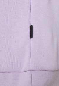 Světlofialový svetr s jemnou pletenou strukturou, s černou štítkovou ozdobou na bočním švu, představující elegantní design.