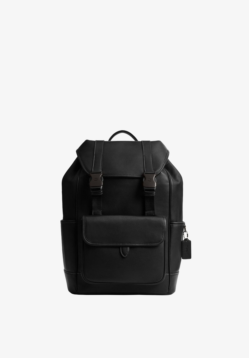 Mustast nahast seljakott ees oleva klapiga, mis on kinnitatud kahe pannaliga rihmaga, suur eesmine tasku ja ülemine käepide valgel taustal.