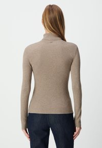 Beige ribgebreide coltrui met lange mouwen, een getailleerde pasvorm en een gestructureerd oppervlak, gecombineerd met donkere denim jeans.