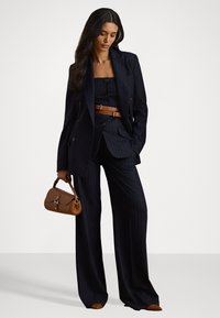Completo blu scuro a righe con pantaloni a gamba larga e top aderente, caratterizzato da un blazer doppiopetto. Accentuato da una cintura marrone e una borsa.