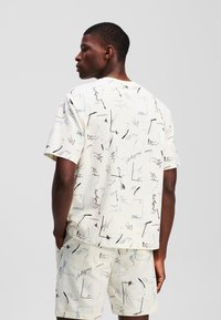 Kortærmet skjorte i let stof og matchende shorts har et abstrakt sort og blåt mønster på en cremefarvet baggrund.