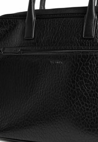 Schwarze Ledertasche mit strukturierter Oberfläche, zwei Griffen und einer vorderen Reißverschlusstasche. Mit silbernem Logodetail und glatten Metallbeschlägen.