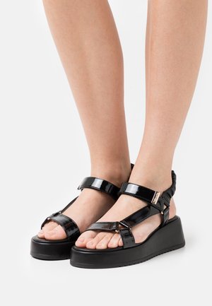 Zwarte lakleren sleehaksandalen met twee verstelbare banden, een gewatteerd voetbed en een gestructureerde zool. Minimalistisch ontwerp met een strakke afwerking.