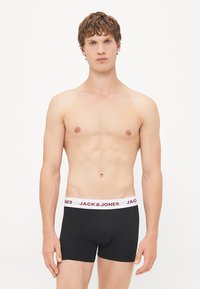 Schwarze Herren-Boxershorts mit einem weißen Bund, versehen mit "JACK & JONES" in roten Buchstaben; glatte Textur, enganliegendes Design.
