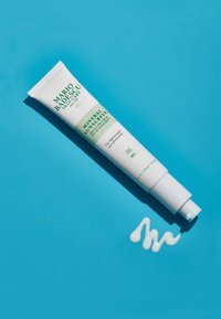 Vit tube med grön text märkt "Mineral Solkräm SPF 30" mot en turkos bakgrund. En liten mängd vit kräm dispenceras.