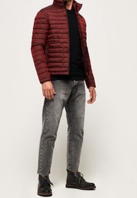 Vínová péřová bunda s vodorovným prošíváním, černé tričko s kulatým výstřihem, šedé zúžené džíny a černé šněrovací boty s detaily.