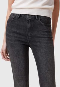 Jeans negros de talle alto con una textura suave, que cuentan con bolsillos delanteros y un diseño clásico de cinco bolsillos. Detalle de costura sutil.