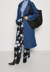 Dżinsowy płaszcz trencz, jasno niebieski golf, czarne spodnie w kwiaty oraz czarne botki na obcasie. Duża czarna torba typu tote dopełnia stylizację.