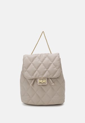 Sac à main beige matelassé avec poignée chaîne dorée et fermeture à verrouillage doré sur le rabat avant sur fond uni.