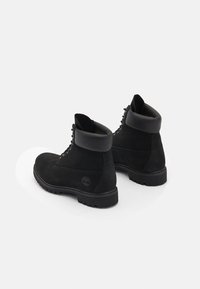 Botas de tobillo de ante negro con un suave cuello de cuero negro, puntera redonda y suela de goma resistente. Presenta el icónico logotipo en el costado.