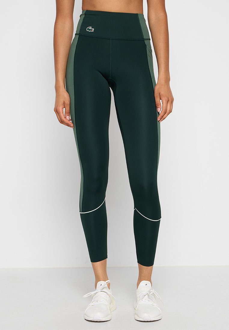 Leggings taille haute, verts foncés, avec des panneaux latéraux vert clair et des coutures blanches d'accent. Tissu lisse et extensible. Logo Lacoste sur la taille.